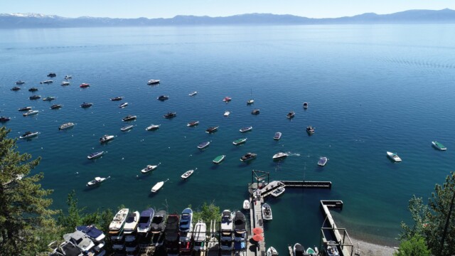 Lake Tahoe from the hillside — Homewood Marina dry stack and a busy day on the water Elevated view of Homewood Marina dry stack and dozens of moored boats on deep blue Lake Tahoe with snow-capped Sierra Nevada mountains