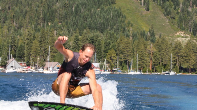 Catching air — wake surf trick on Lake Tahoe's west shore Man wake surfing an aerial trick on a green board on Lake Tahoe with pine-covered mountain backdrop