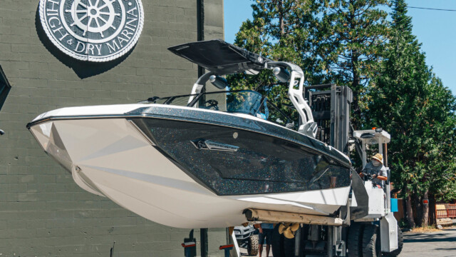 Moving day at Homewood — the black Nautique gets its turn. A forklift moves a black glitter Super Air Nautique outside Homewood High & Dry Marina, the marina's ship wheel logo prominent on the wall.