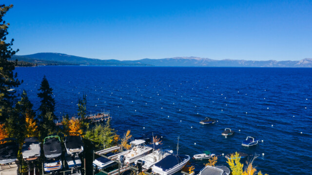 Lake Tahoe in fall — marina dry stack, mooring buoys, and deep blue water under clear skies. Elevated view of Lake Tahoe marina with dry-stacked boats, mooring buoys, fall foliage, and mountain backdrop