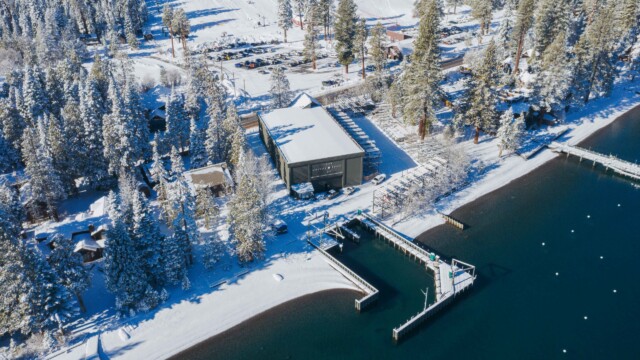 Homewood Marina in winter — snow-covered pines, docks, and deep blue Lake Tahoe from above Aerial winter view of Homewood Marina on Lake Tahoe surrounded by snow-covered pine trees and docks